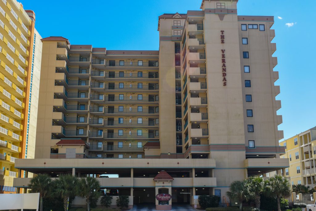 Front view of The Verandas in North Myrtle Beach is a beachfront resort featuring balconies and a palm tree-lined entrance.