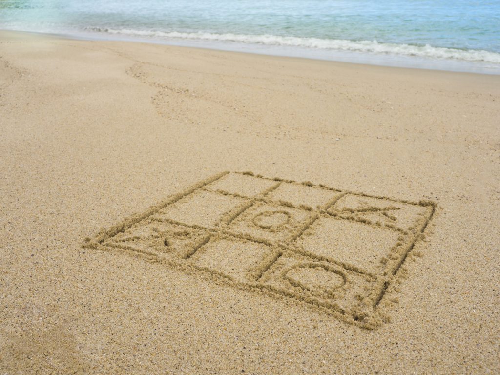 a tic-tac-toe board drawn into the sand with the ocean waves in the background